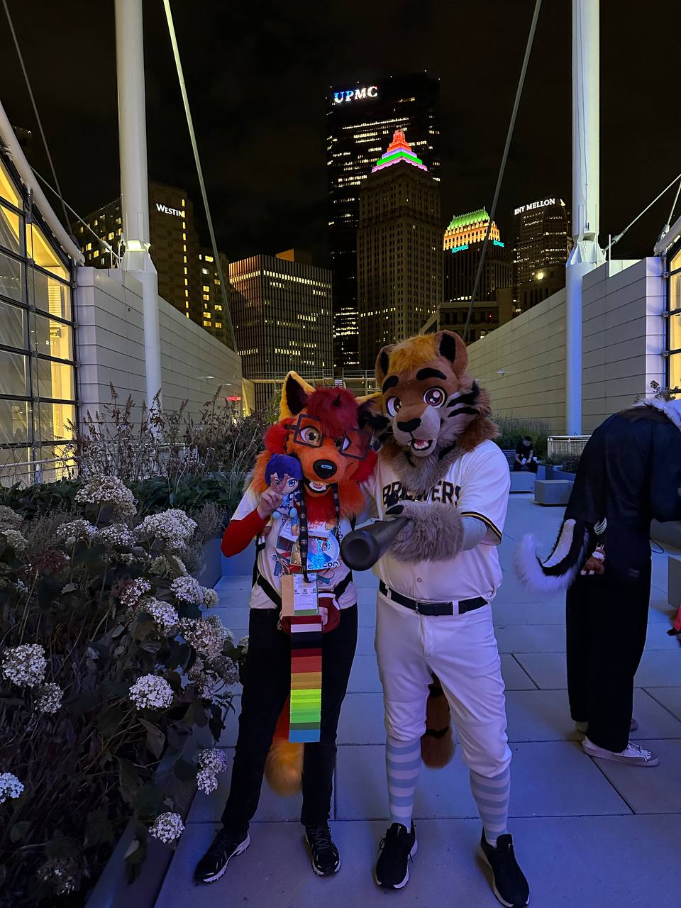 Lexicon and Tugo (tiger fursuiter with Milwaukee Brewers attire and a baseball bat) posing on the DLCC rooftop at night